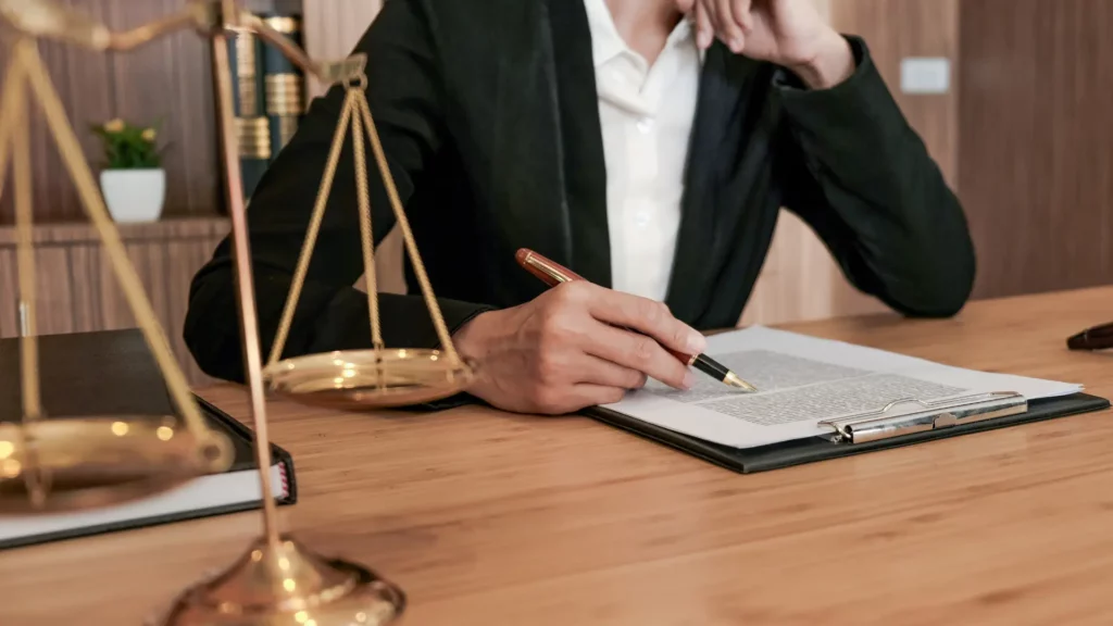 Person reviewing legal documents at a desk with a justice scale, in a professional law office setting.